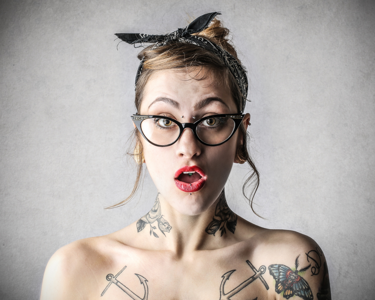 Удивленная девушка в очках с татуировками на теле