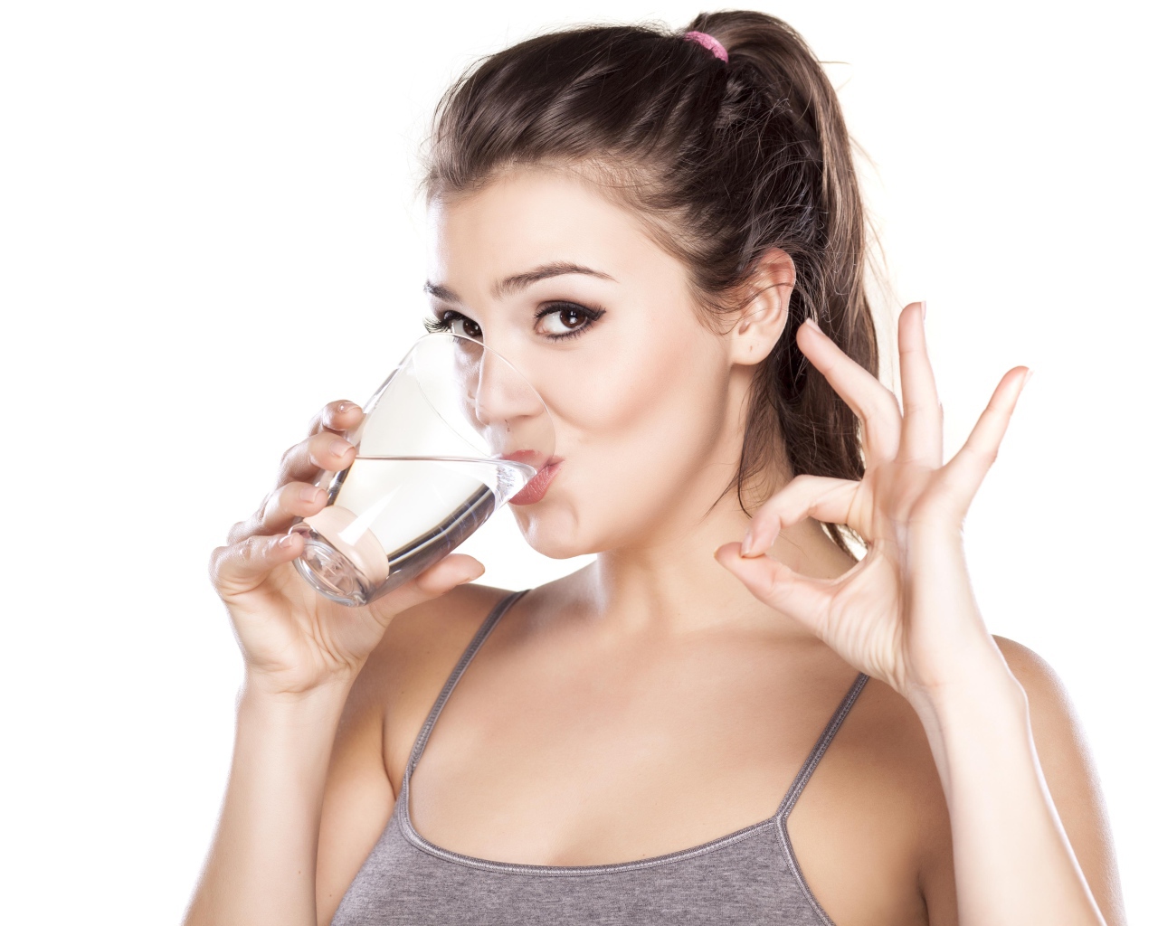 Молодая спортивная девушка пьет воду из стакана
