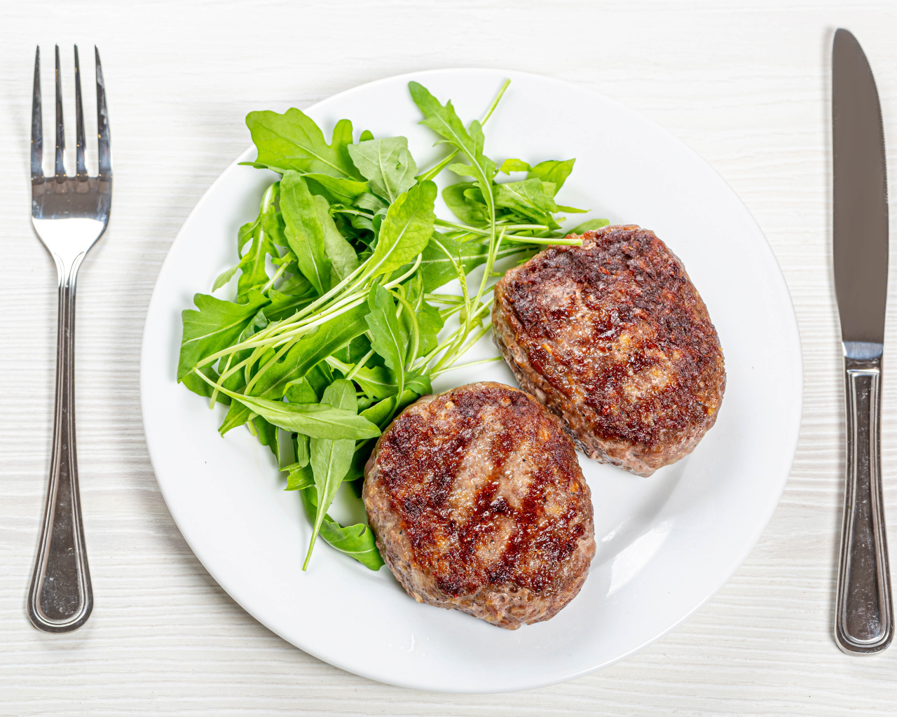 Две котлеты на тарелке с зеленью рукколы 