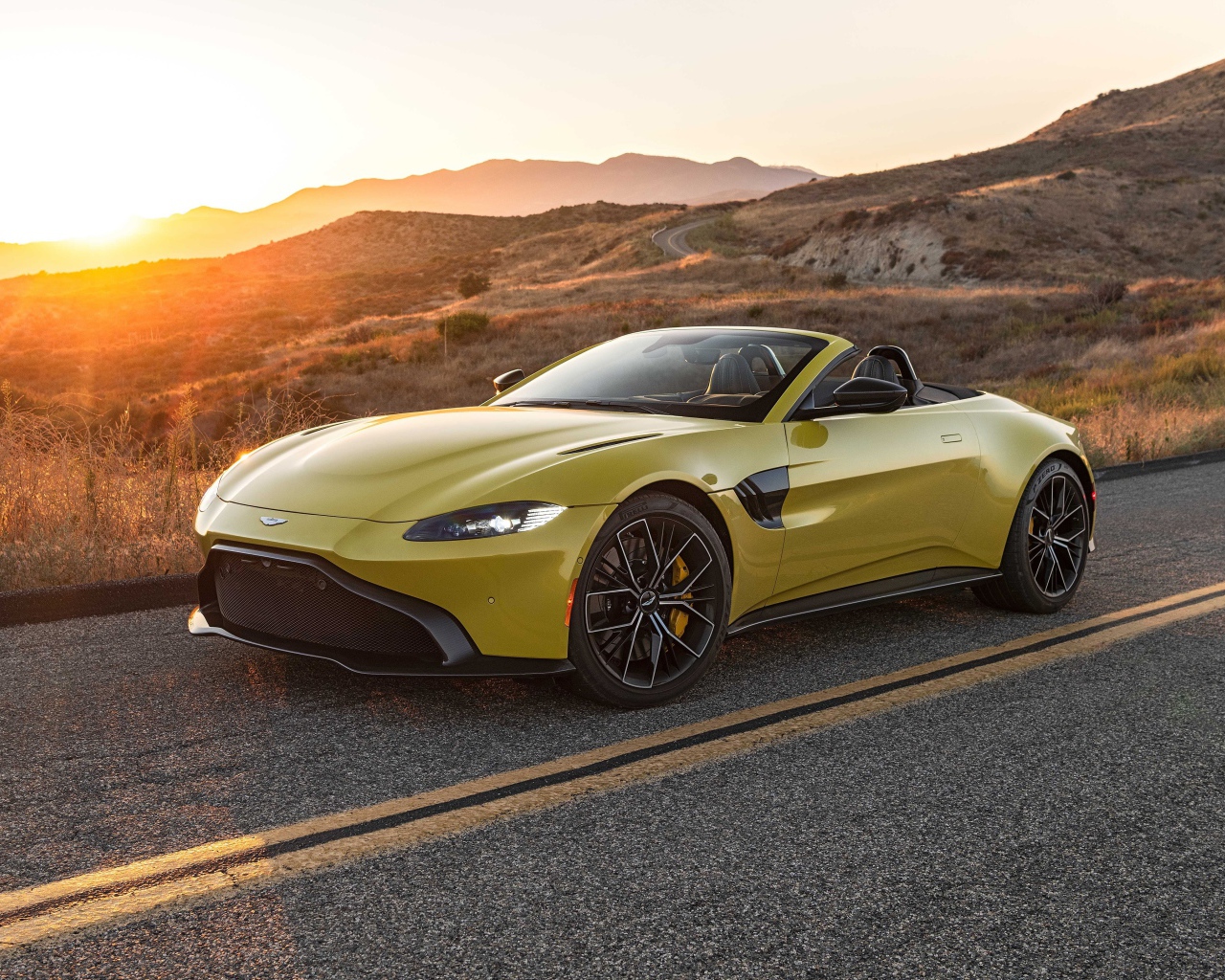 Желтый кабриолет  Aston Martin Vantage Roadster, 2021 года на трассе на рассвете