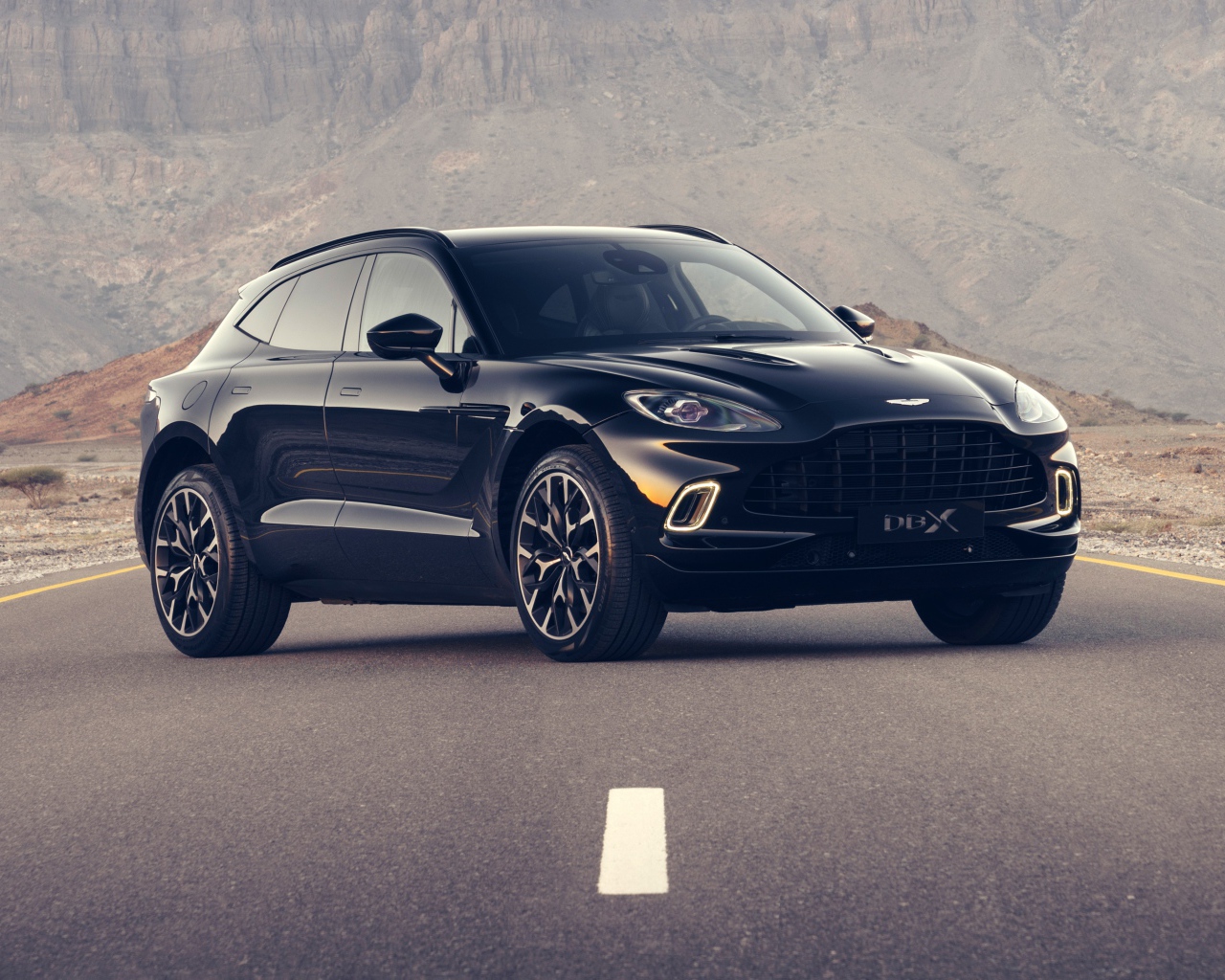 Черный автомобиль aston Martin DBX 2020 года на трассе в горах