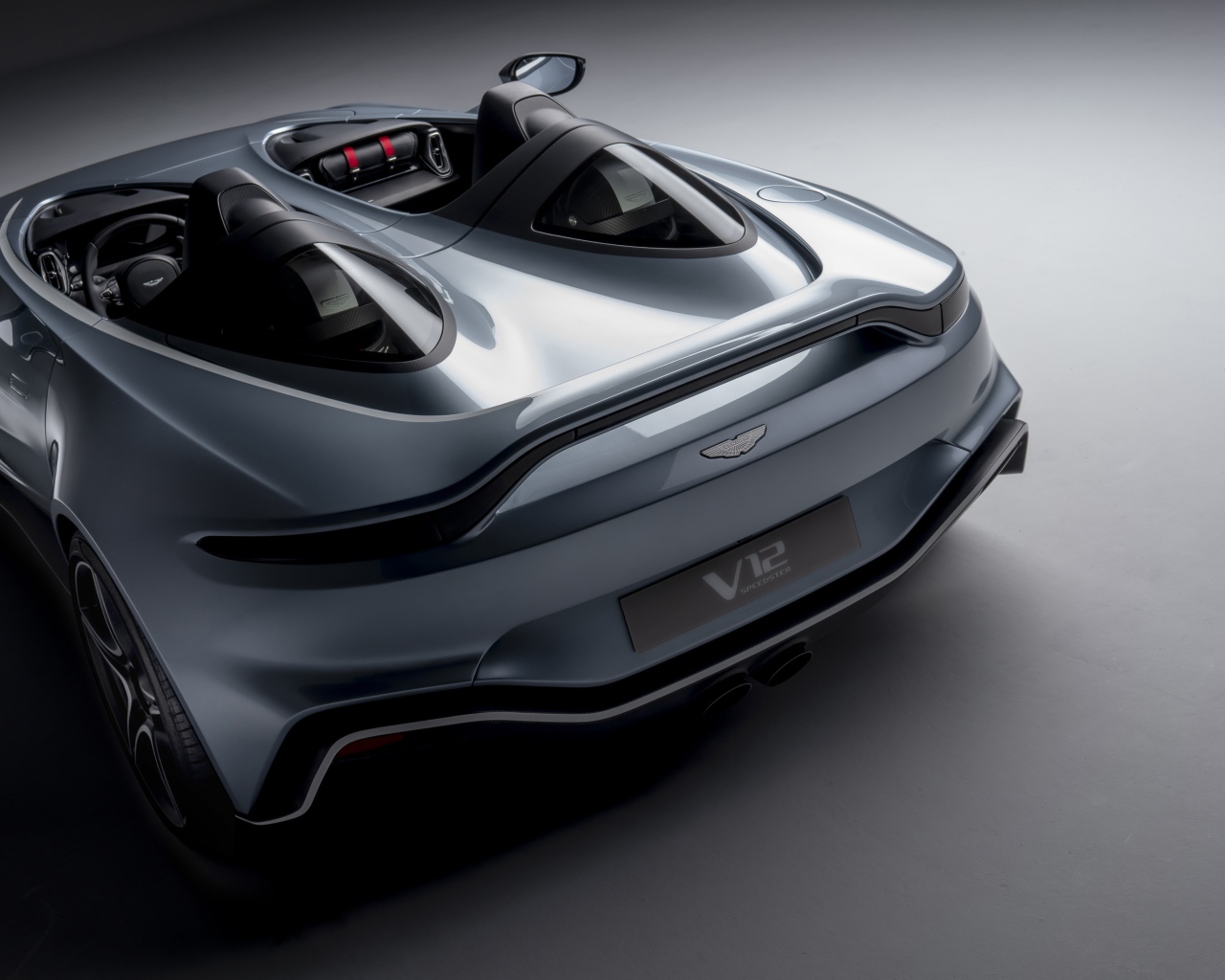 Серебристый автомобиль Aston Martin V12 Speedster 2020 года на сером фоне вид сзади
