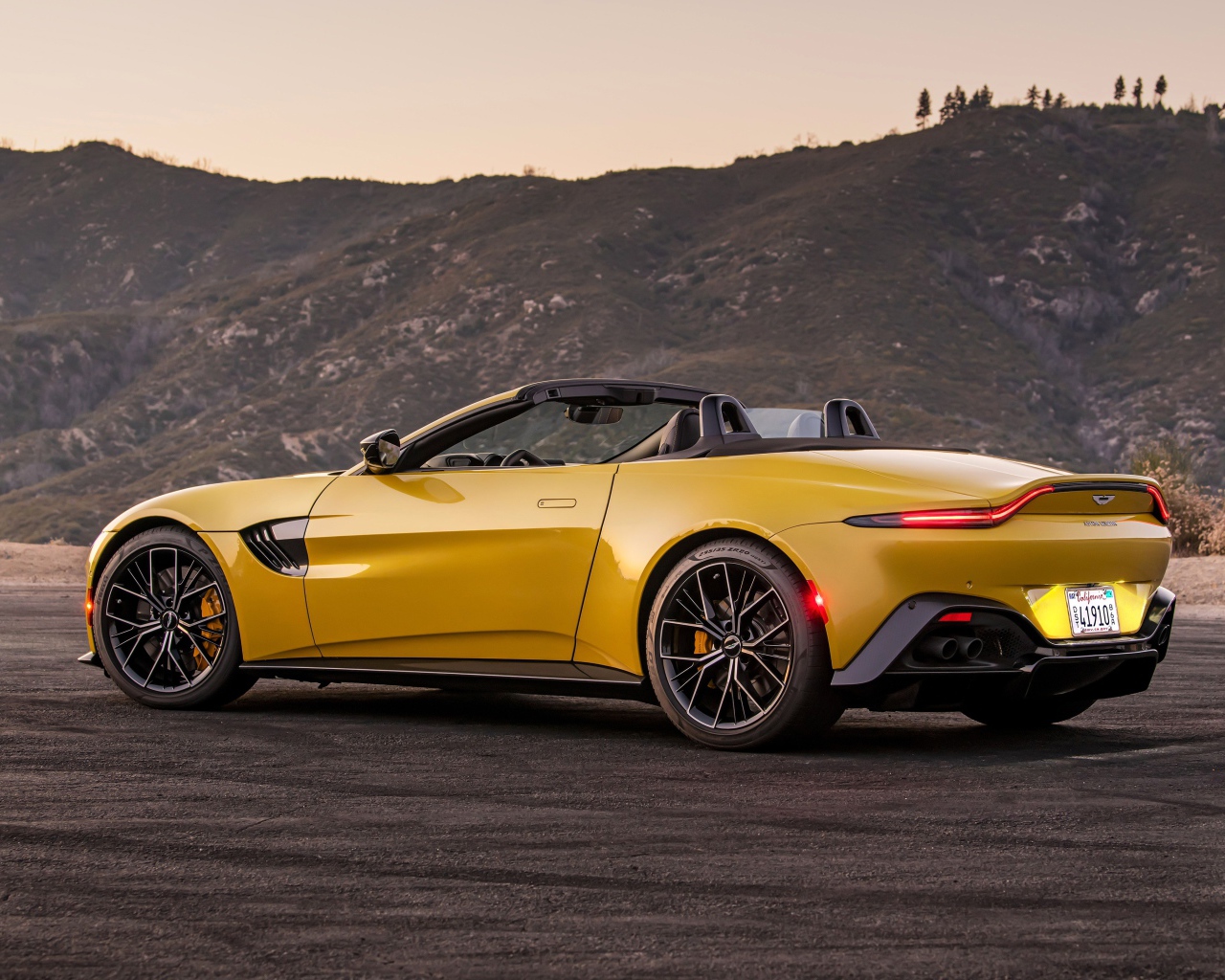 Желтый автомобиль  Aston Martin Vantage Roadster, 2021 года на фоне гор 