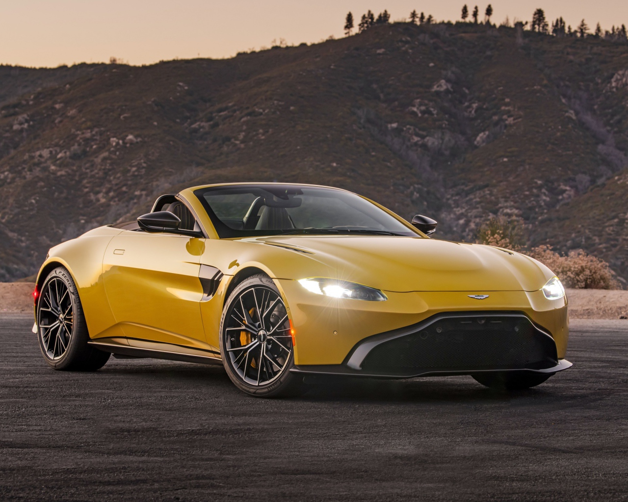 Желтый автомобиль  Aston Martin Vantage Roadster, 2021 года на фоне холмов