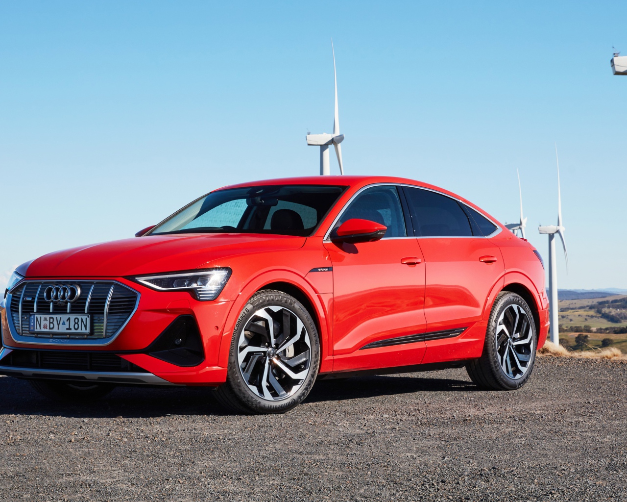Красный автомобиль Audi E-Tron 50 Quattro Sportback S Line 2020 на фоне ветряных турбин