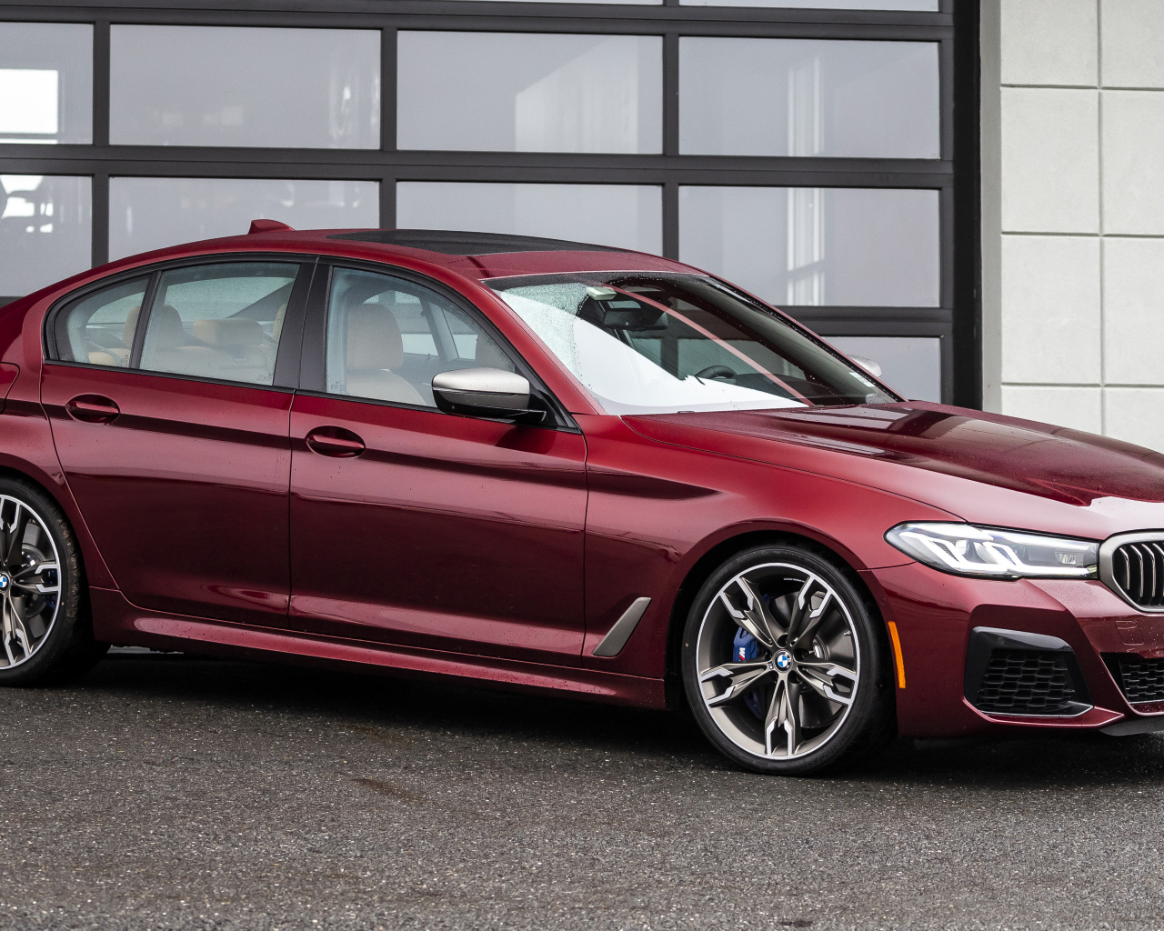 Красный автомобиль BMW M550i XDrive, 2021 года у гаража