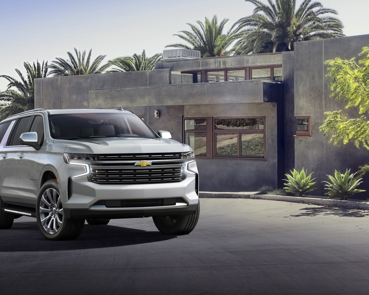 Серый внедорожник Chevrolet Suburban, 2021 года на фоне дома
