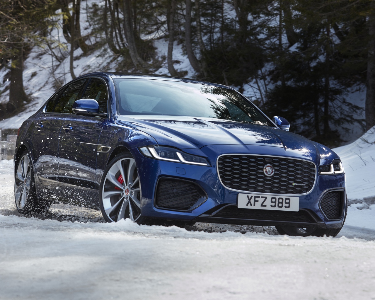 Синий Jaguar XF P300 AWD R-Dynamic 2020 года в заснеженном лесу 