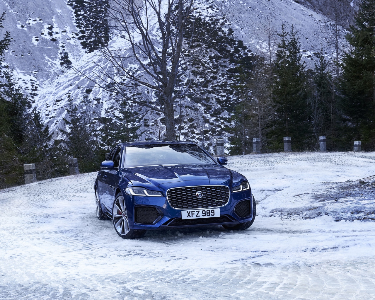 Синий автомобиль Jaguar XF зимой на фоне горы 