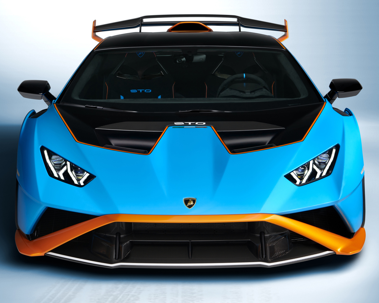 Голубой автомобиль Lamborghini Huracán STO 2021 года вид спереди на сером фоне