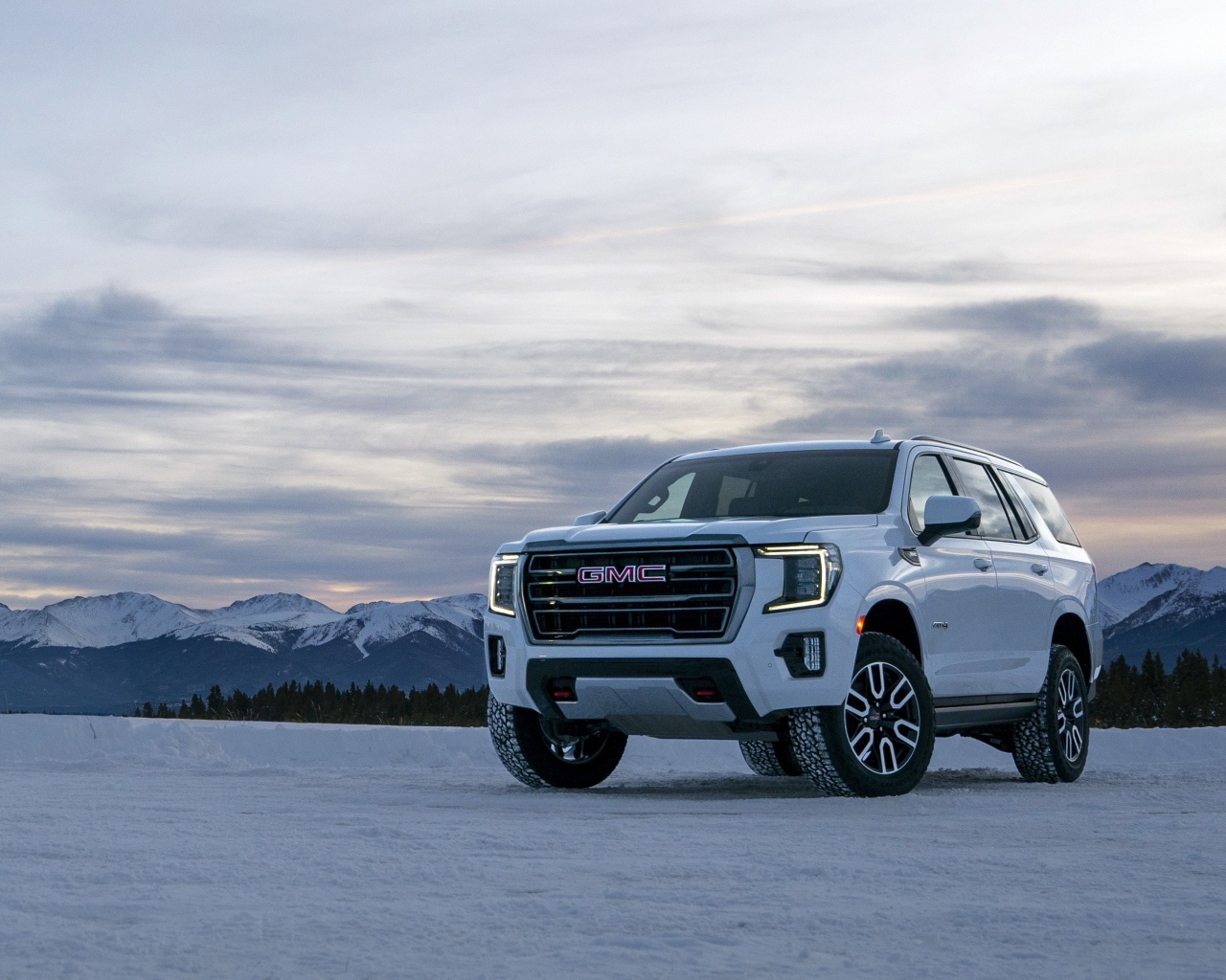 Белый внедорожник  GMC Yukon AT4, 2021 года на фоне заснеженных гор 