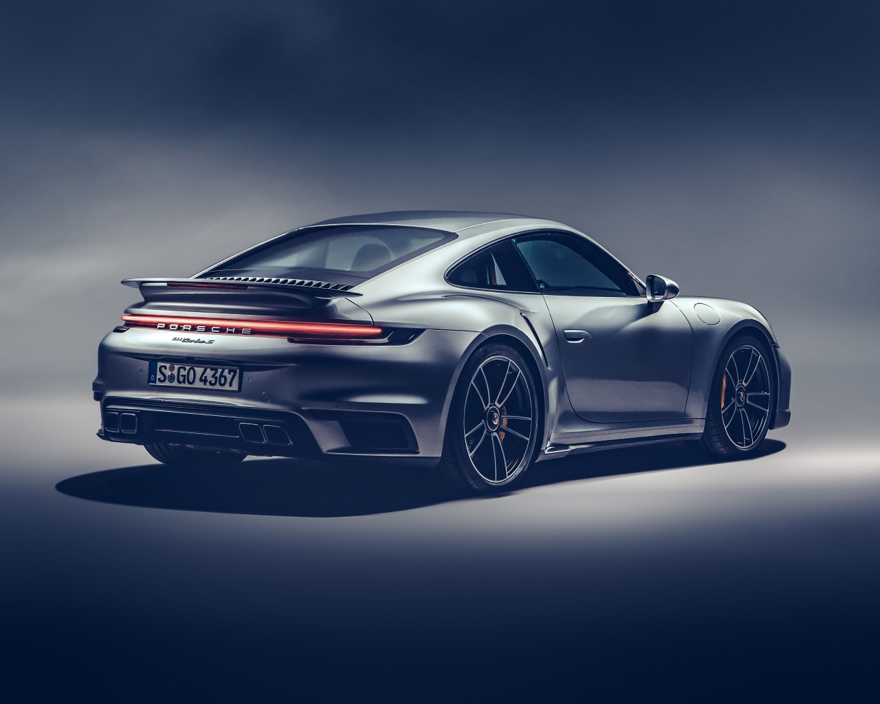 Автомобиль Porsche 911 Turbo S 2020 года на сером фоне вид сзади