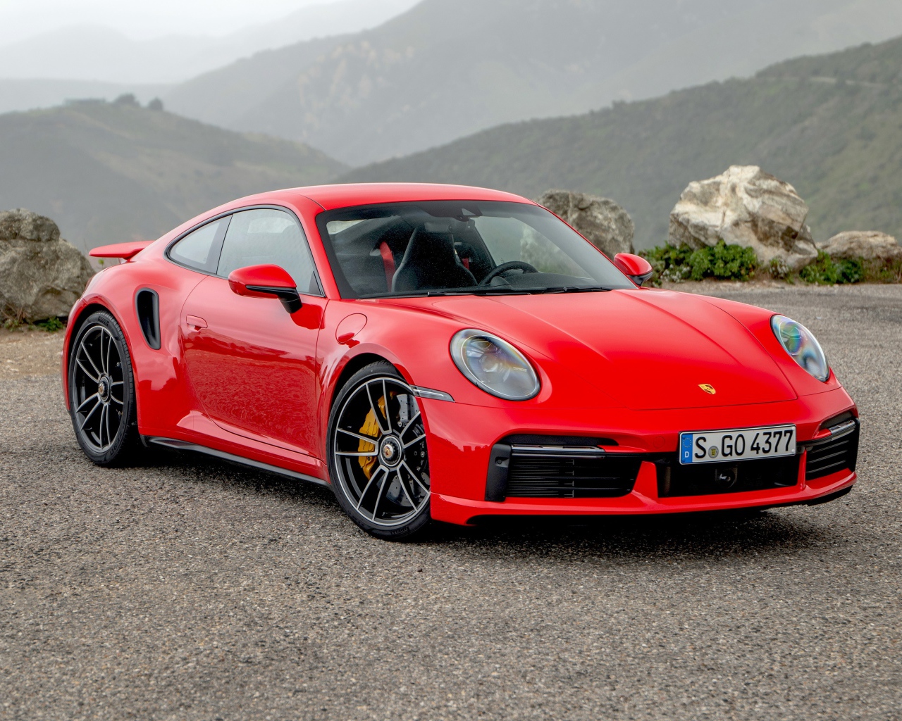 Красный автомобиль Porsche 911 Turbo S 2020 года на фоне гор 