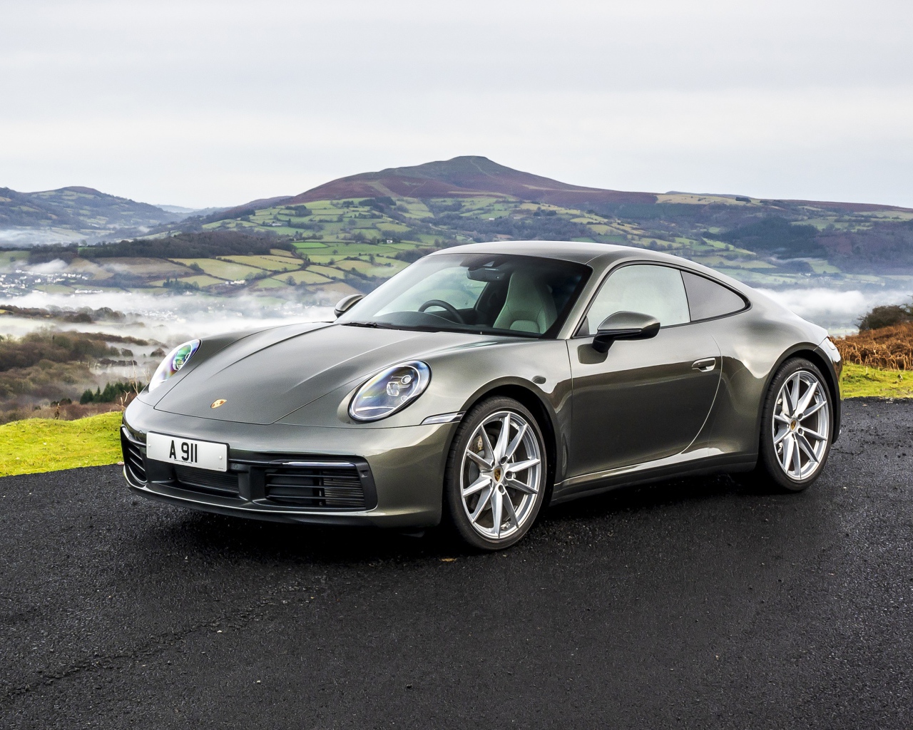 Серебристый автомобиль Porsche 911 Carrera на фоне холмов