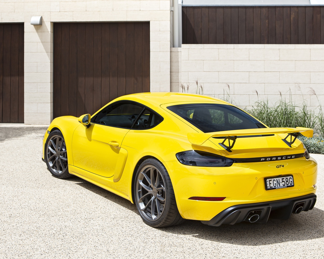 Желтый автомобиль Porsche 718 Cayman GT4, 2020 года у гаража 
