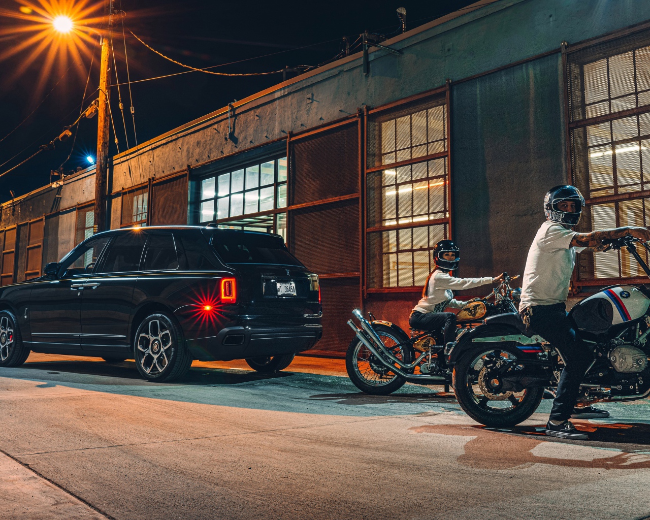 Черный автомобиль Rolls-Royce Cullinan, 2020 года у гаража с байкерами