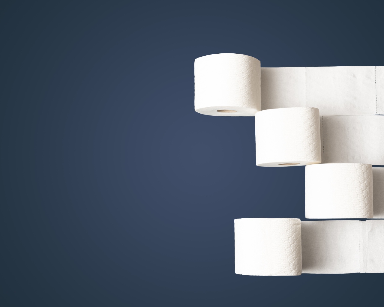 Четыре рулона белой туалетной бумаги на сером фоне