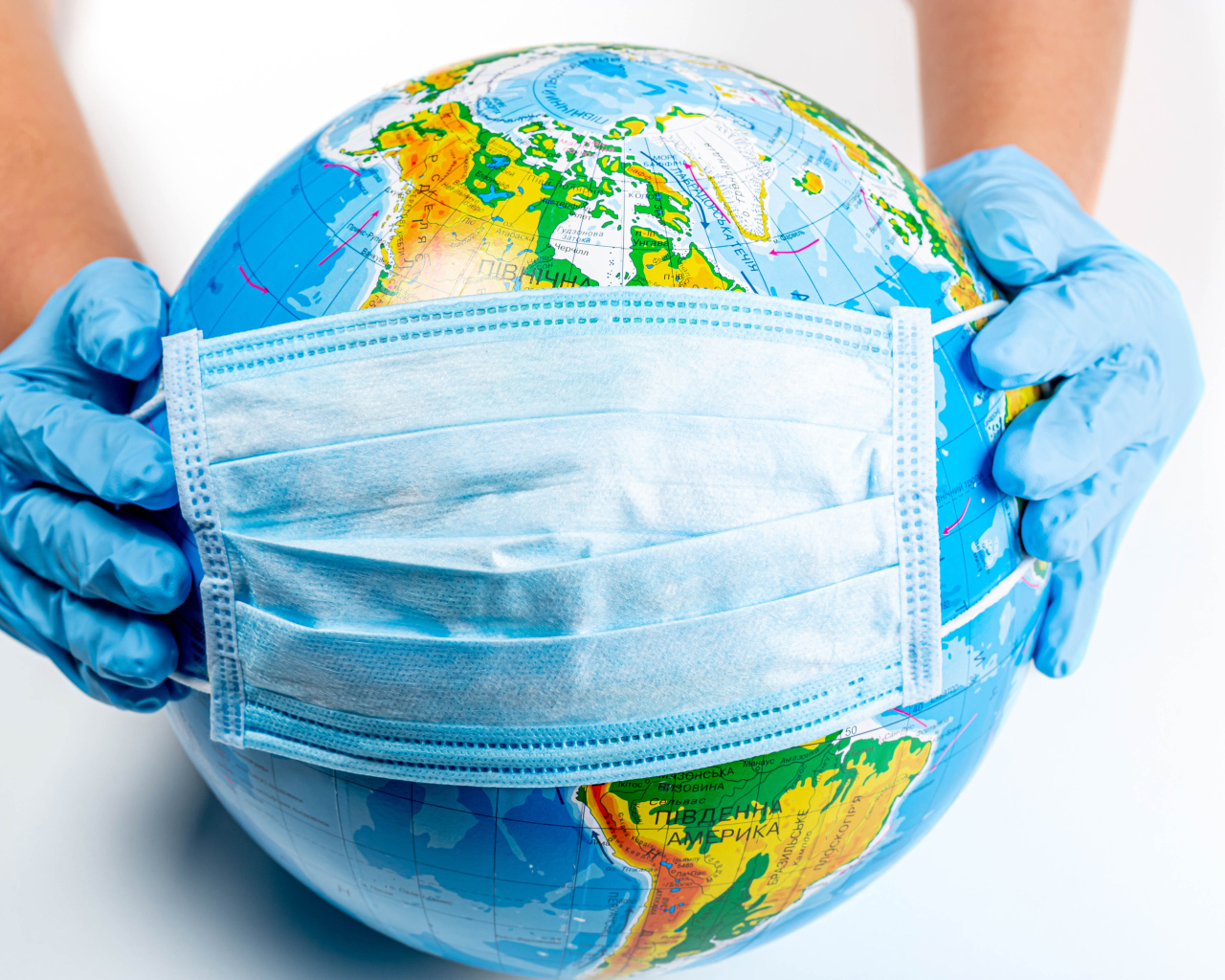 Руки одевают маску от коронавируса на глобус 