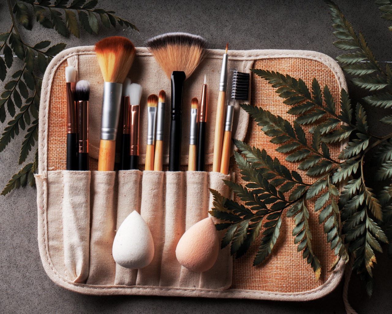 Кисти для макияжа в чехле на столе с листьями папоротника