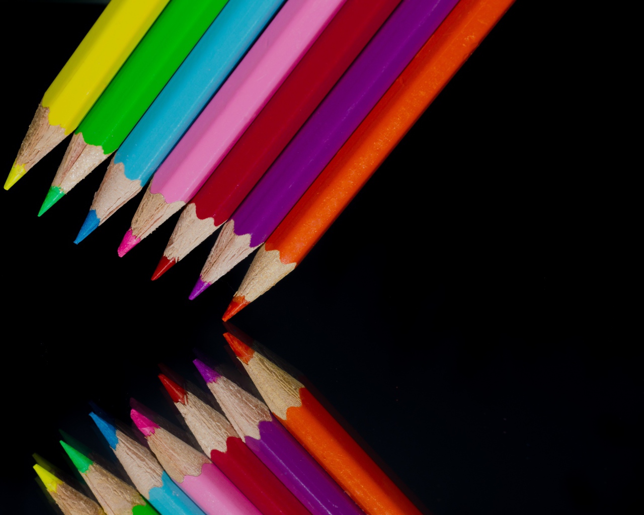 Разноцветные карандаши отражаются в черной зеркальной поверхности 