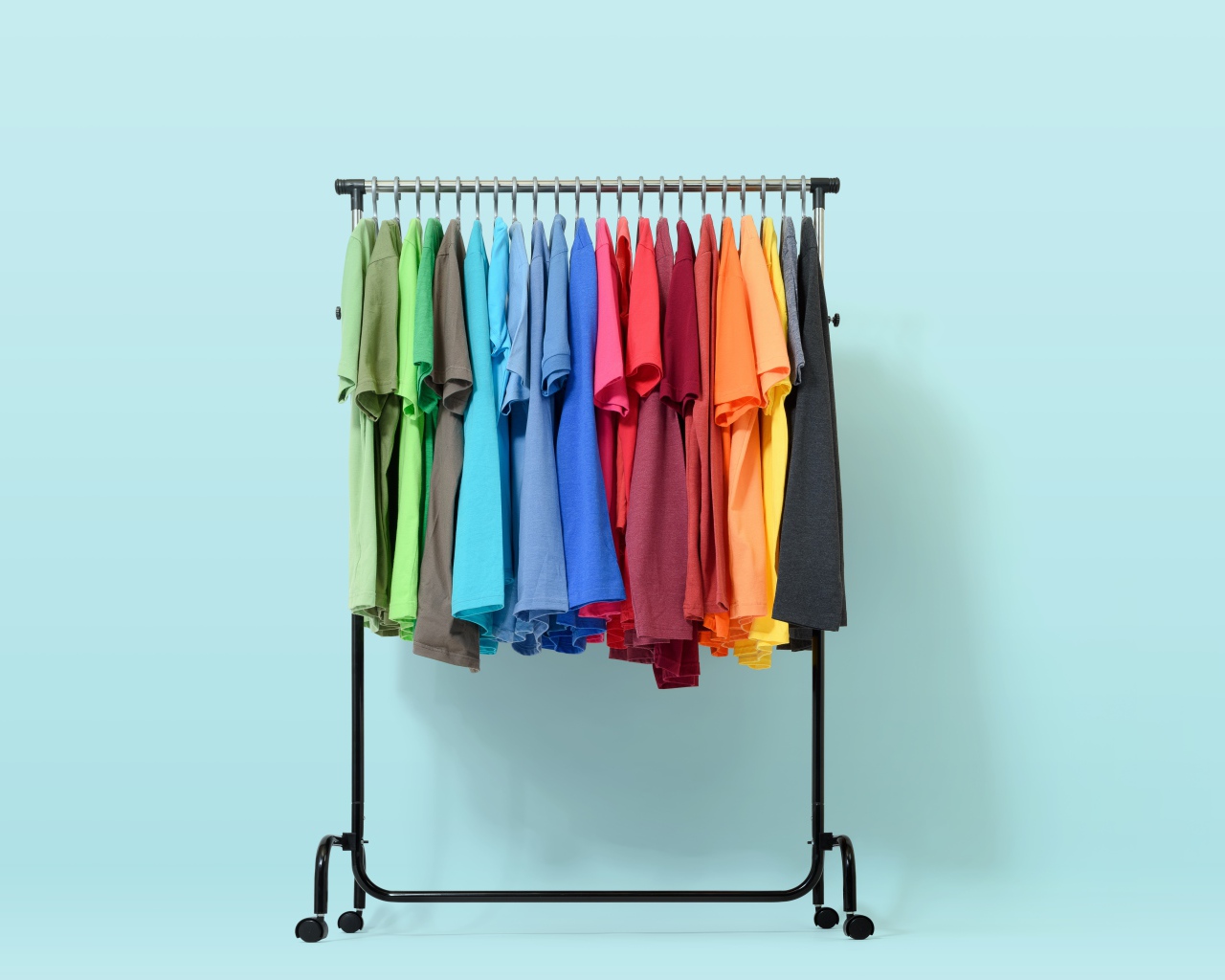 Разноцветные футболки на вешалке на голубом фоне