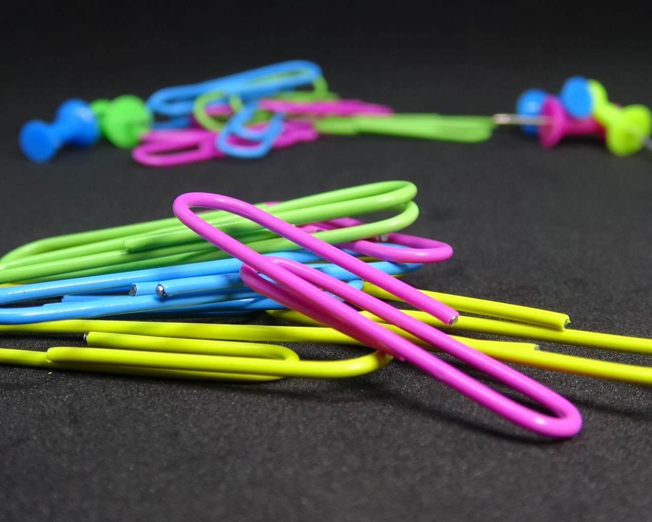 Разноцветные скрепки на черном столе 