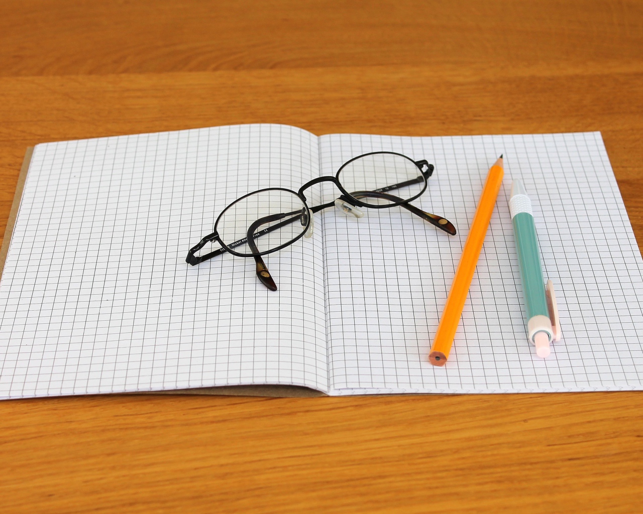 Notebook, pen, pencil and glasses are on the desk