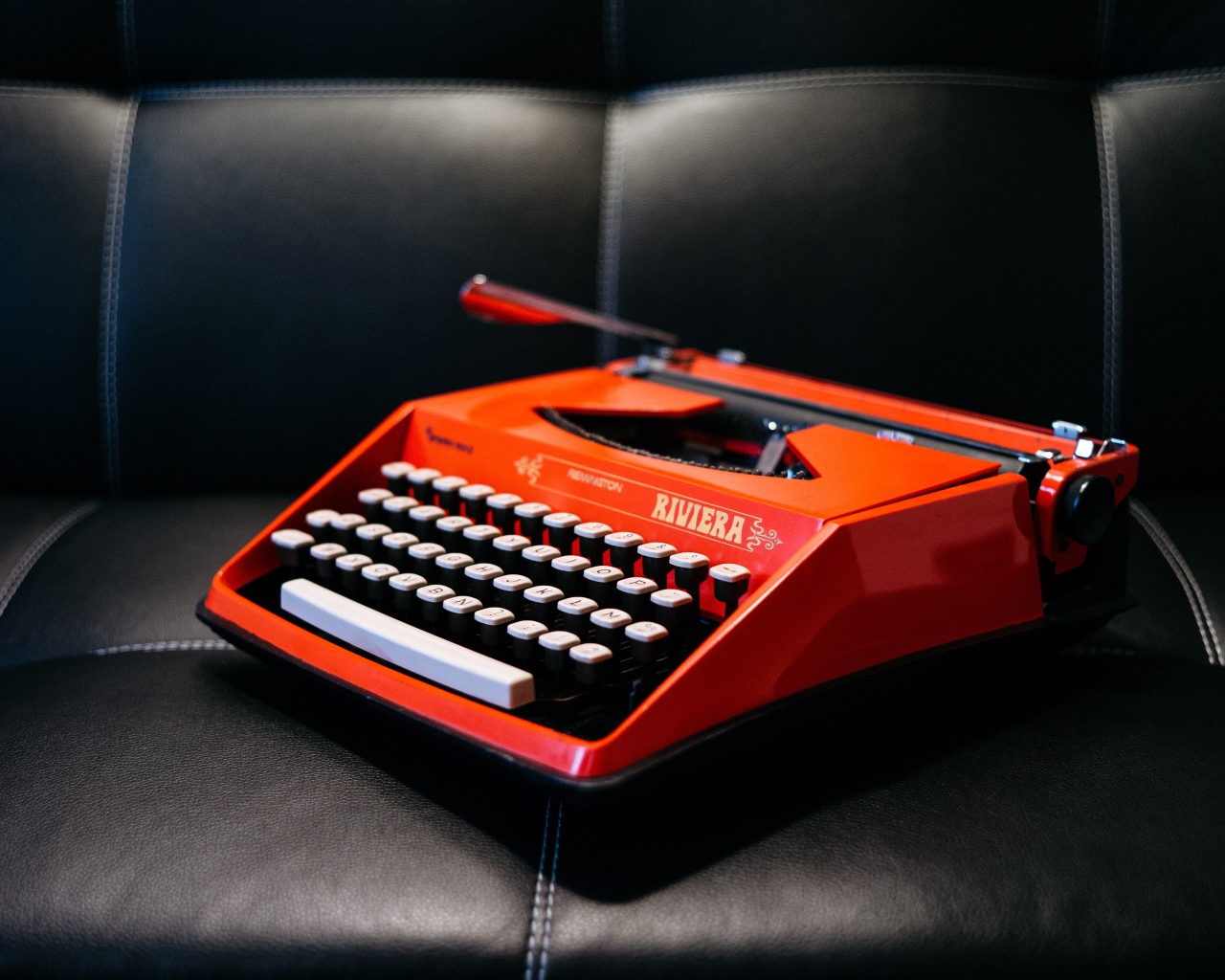 Старая красная печатная машинка на черном диване