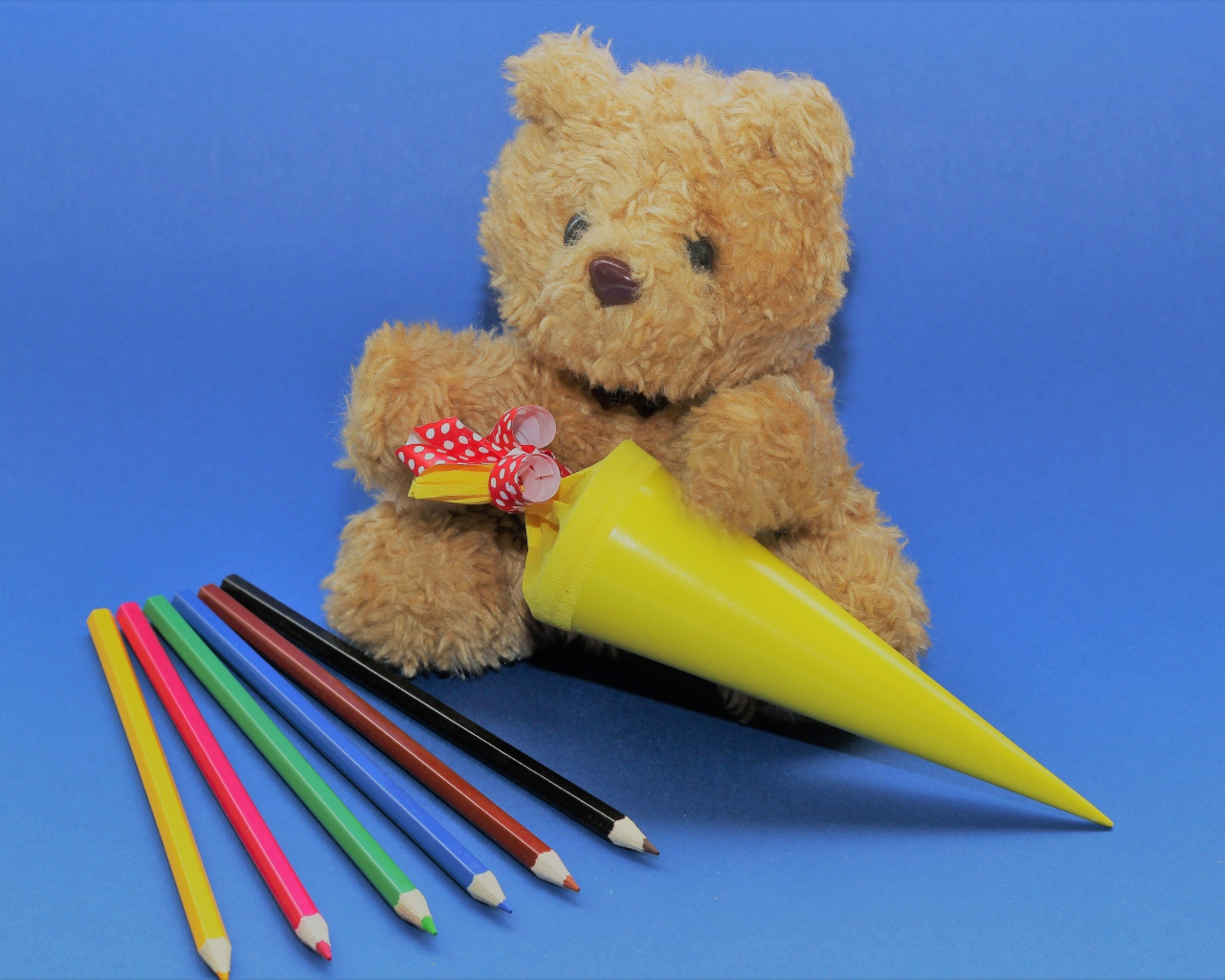 Игрушечный медвежонок  с карандашами на синем фоне