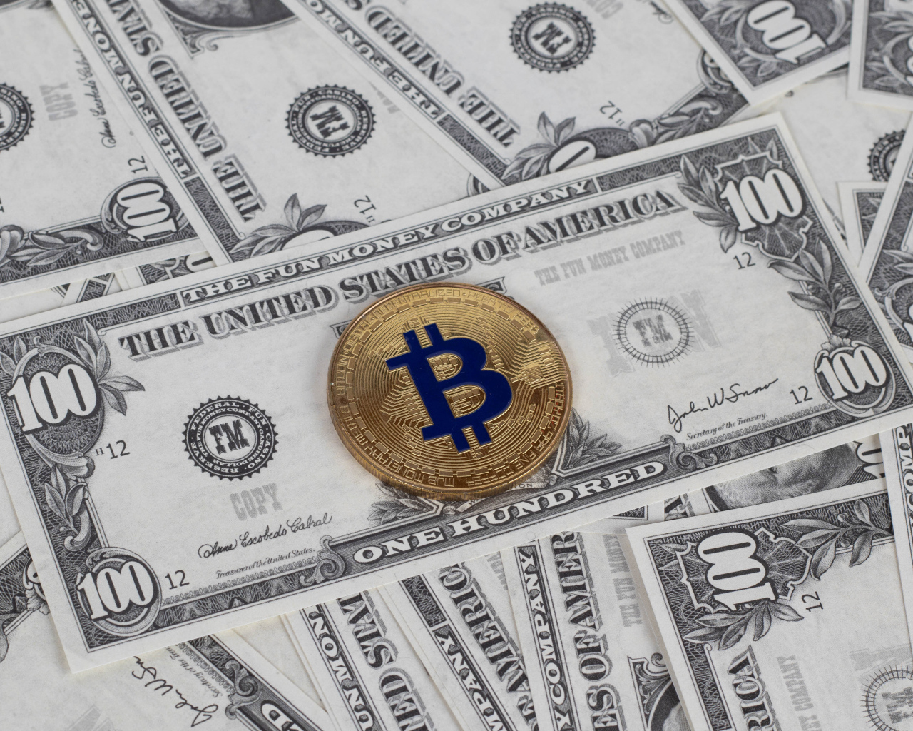 Монета Биткоин лежит на стодолларовых купюрах