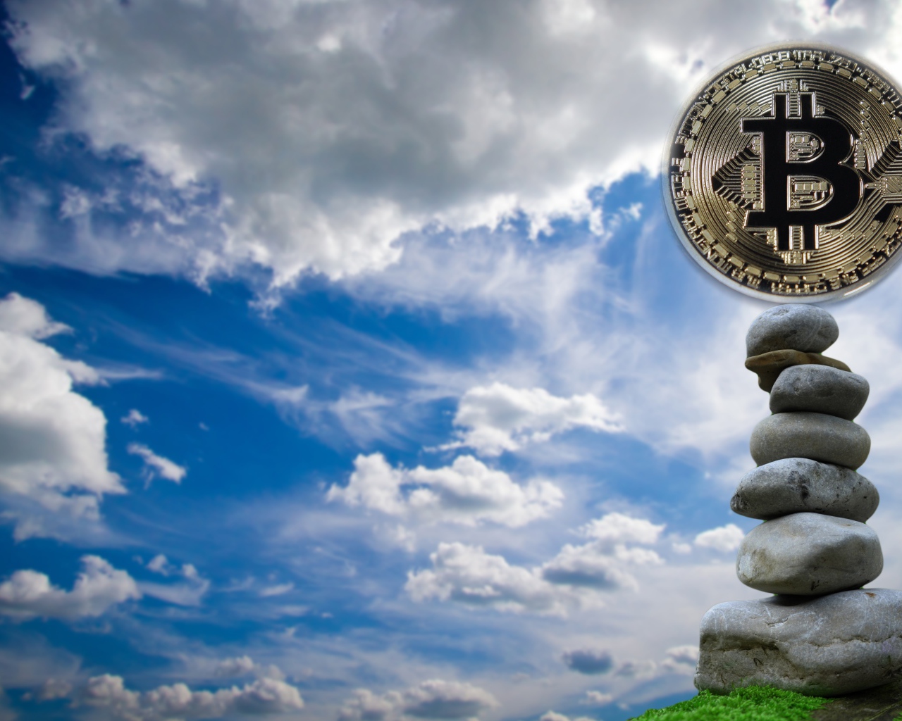 Монета биткоин стоит на камнях на фоне неба
