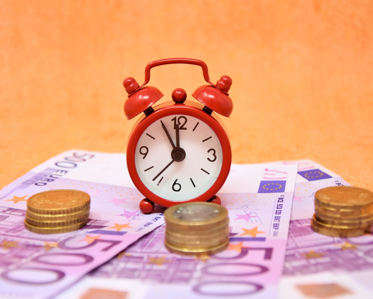 Маленький красный будильник с купюрами евро и монетами