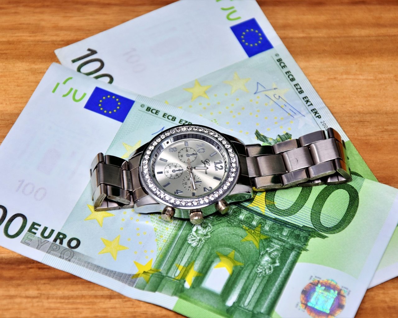 Две купюры по сто евро с часами на столе 