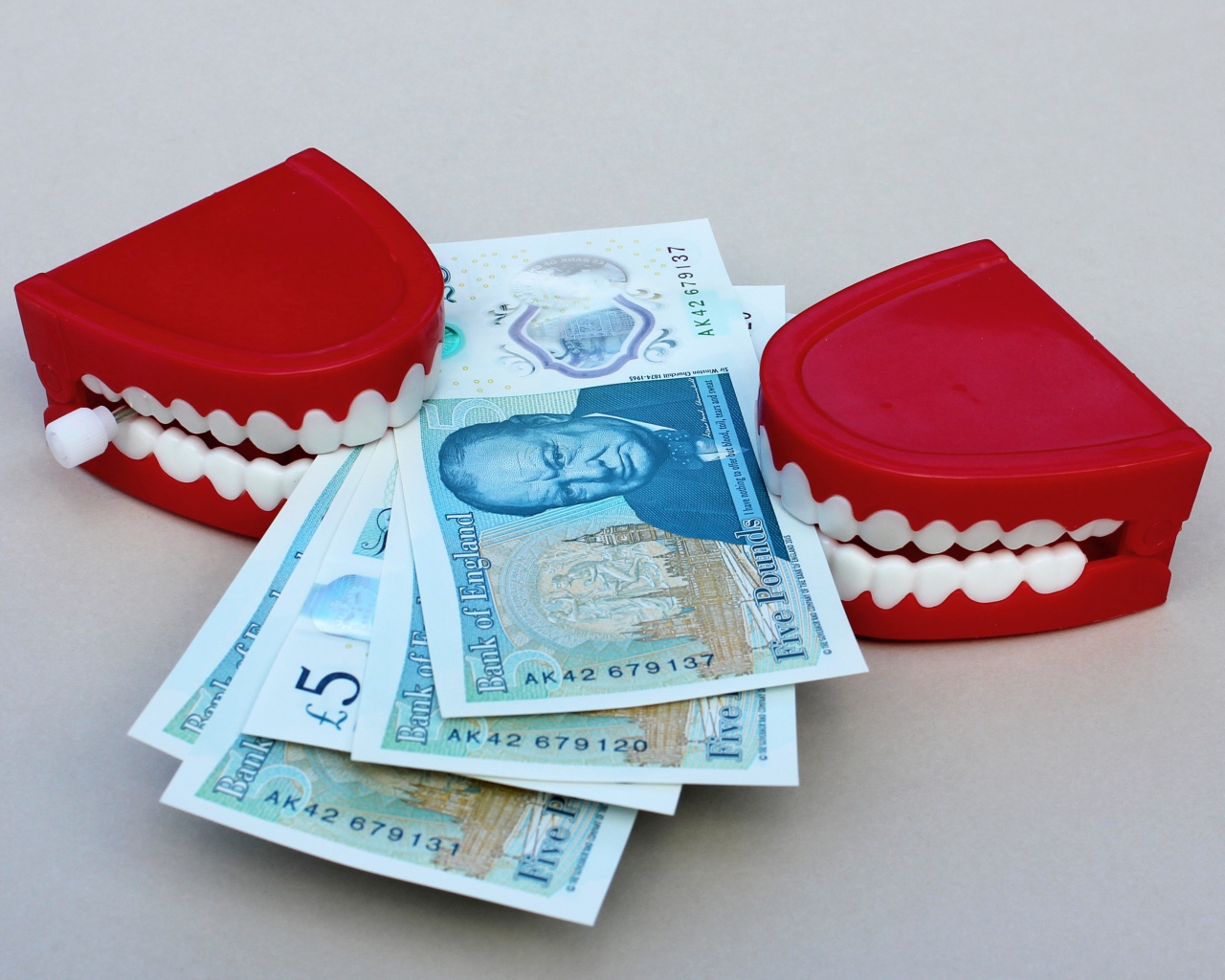Два держателя денег в форме челюсти с купюрами на сером фоне