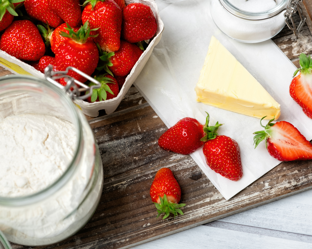 Кусок масла на столе с клубникой и мукой 