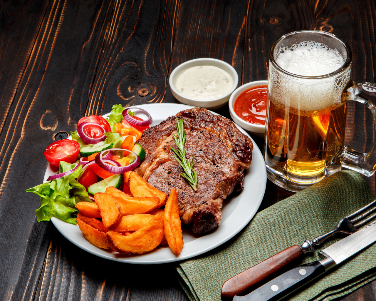 Кусок мяса на тарелке с картофелем и салатом на столе с соусом и пивом