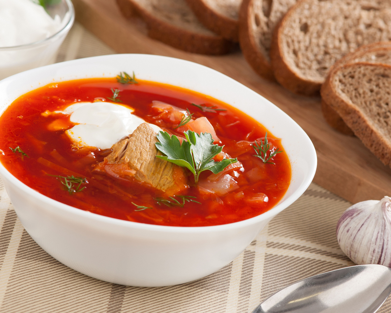 Тарелка горячего борща на столе с хлебом и чесноком