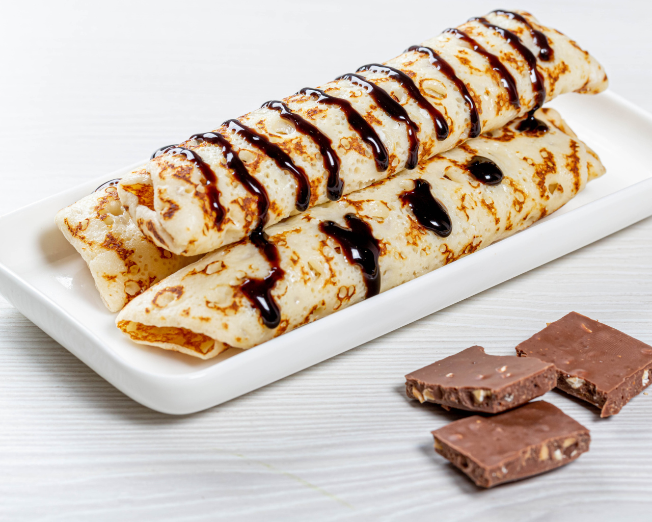 Аппетитные тонкие блины на белой тарелке с шоколадом