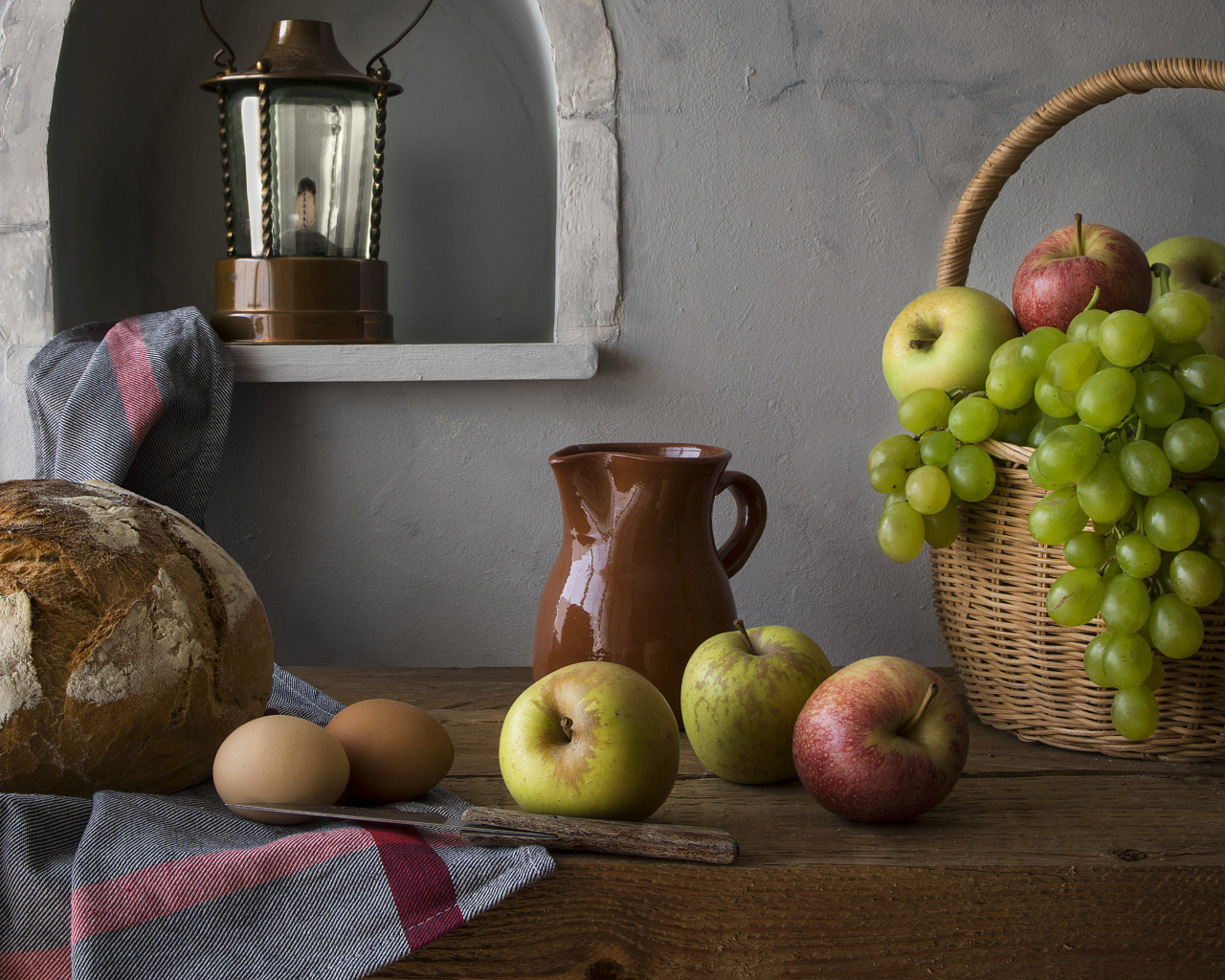 Корзина с яблоками и виноградом на столе с хлебом и яйцами