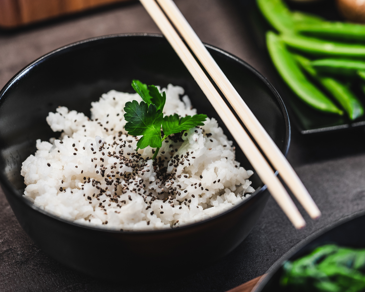 Вареный рис с семенами  в черной миске с палочками