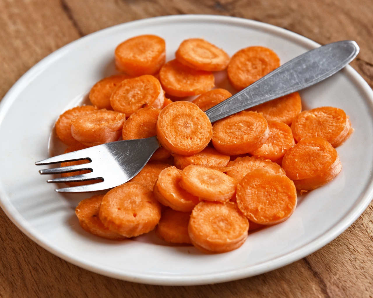 Морковь кружочками на белой тарелке с вилкой