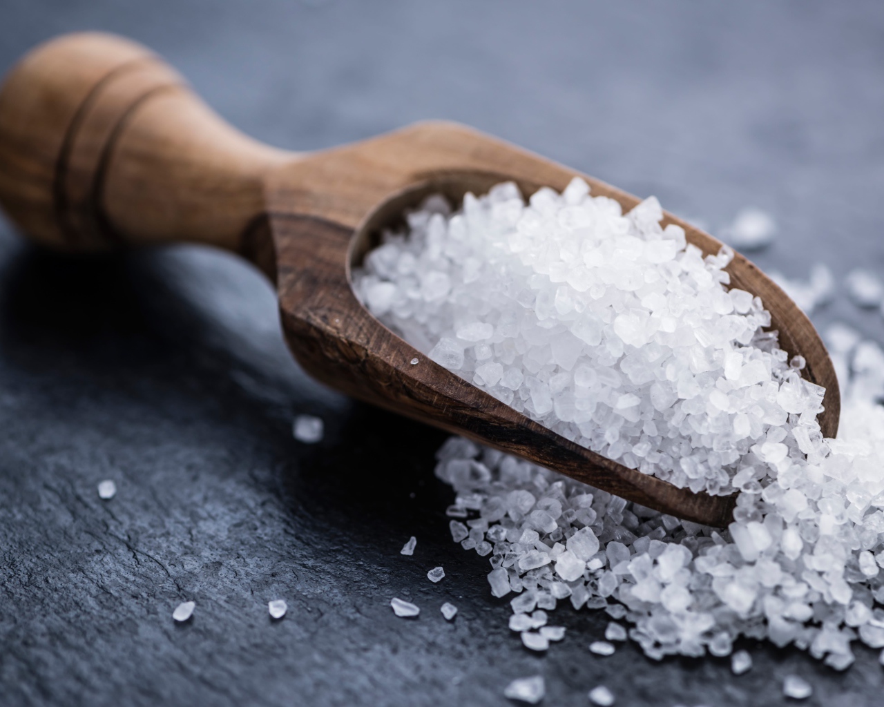 Крупная белая соль в лопатке на столе 