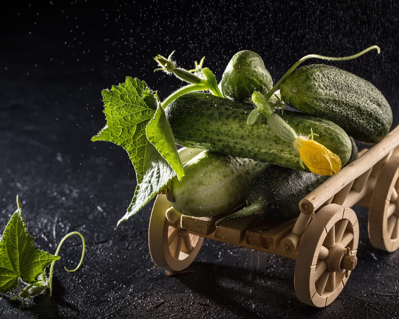 Огурцы на игрушечной тележке на черном столе