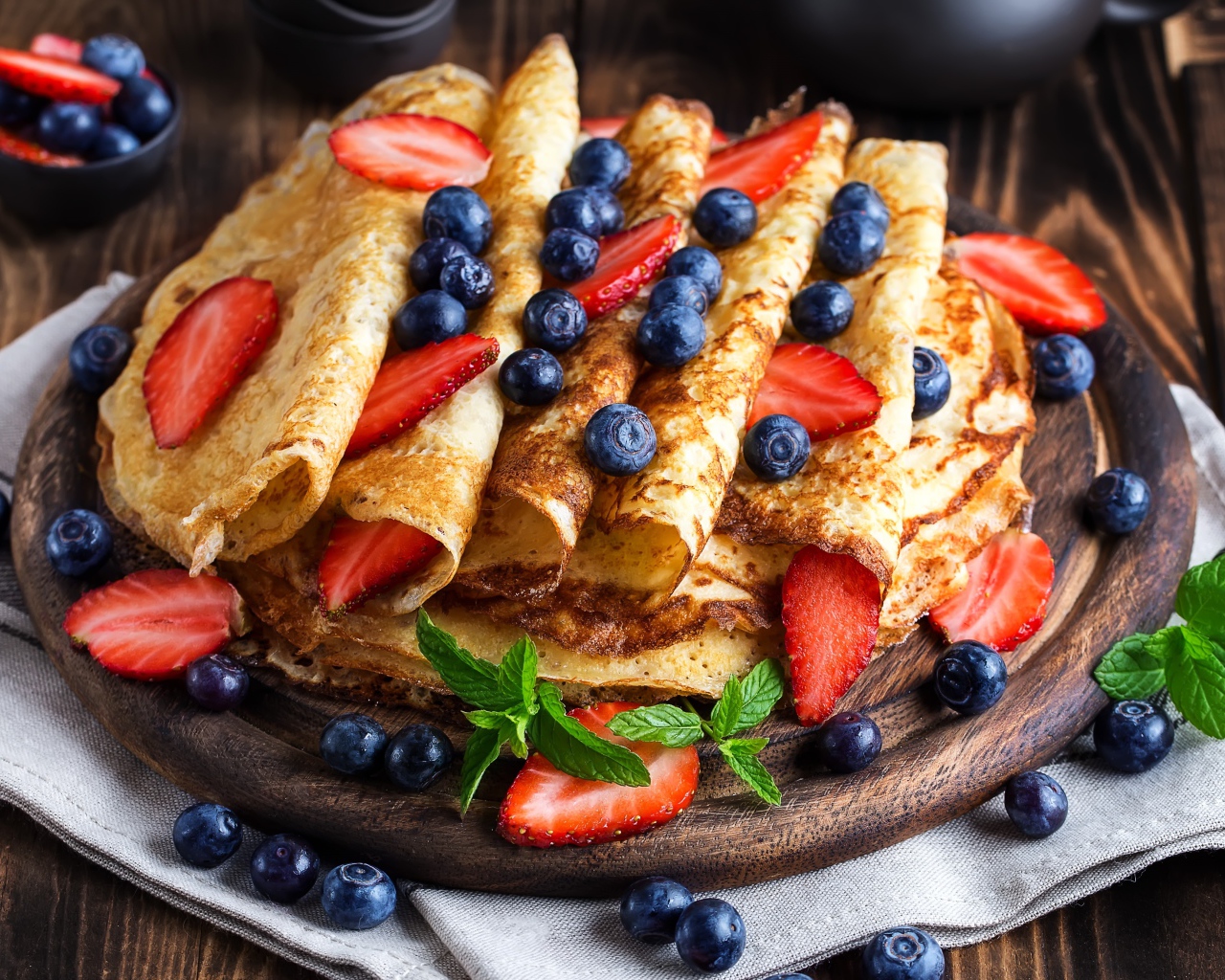 Вкусные тонкие блинчики на деревянной доске с ягодами черники и клубники 