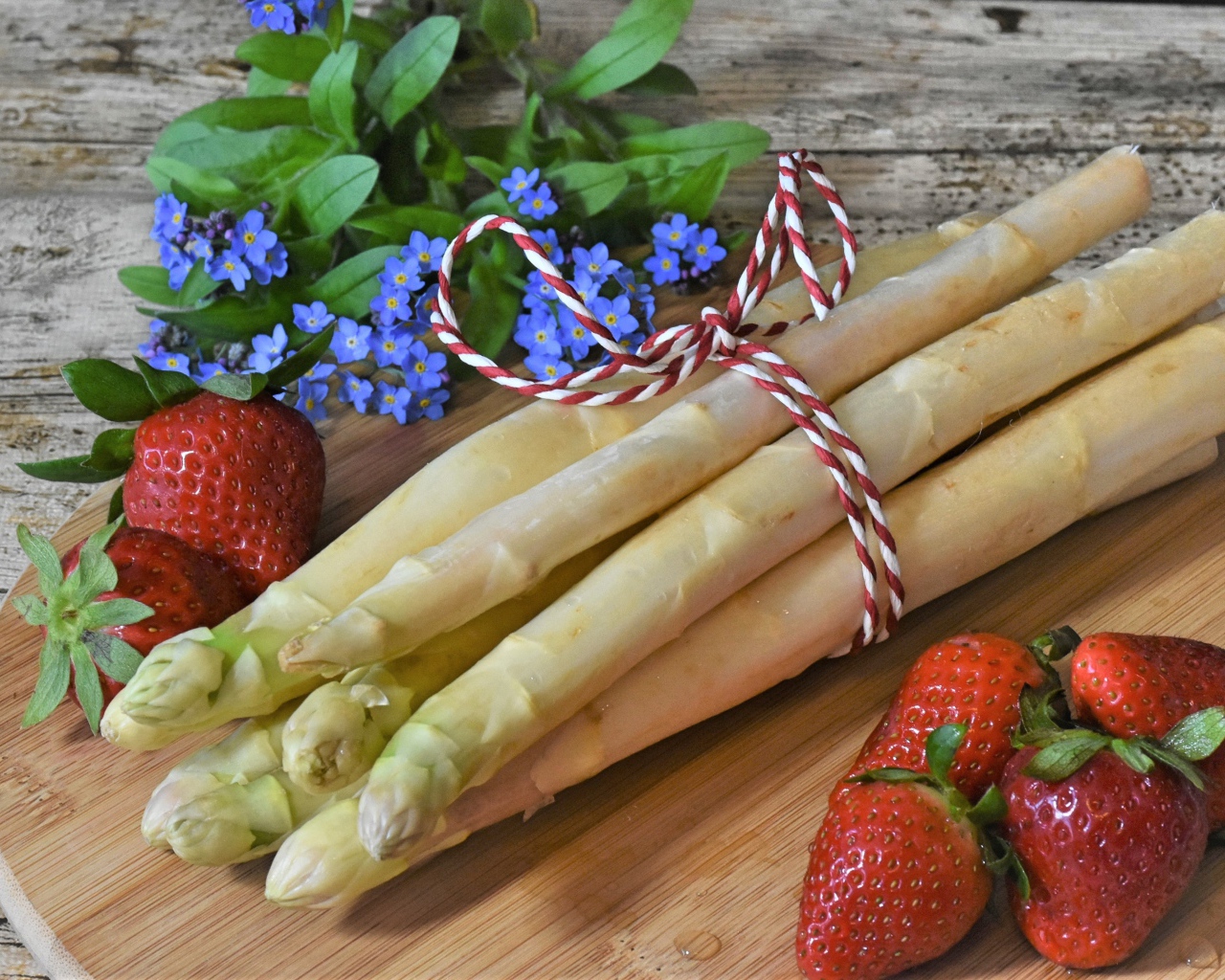 Свежая спаржа на столе с клубникой и цветами незабудками