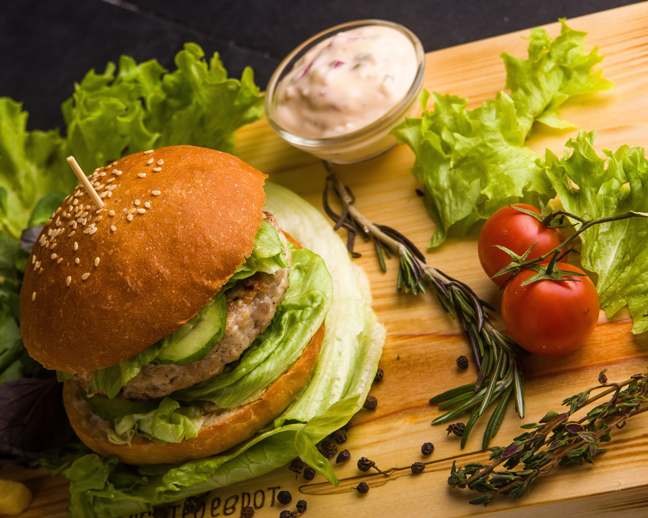 Гамбургер на столе с листьями салата, специями, помидорами и соусом