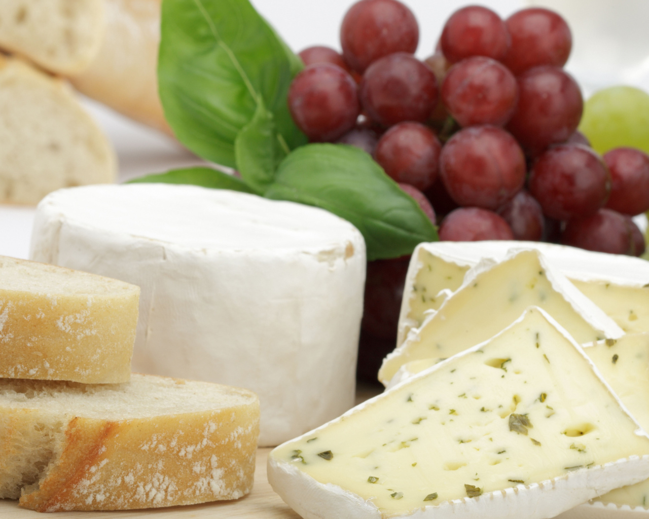 Твердый сыр на столе с батоном и виноградом