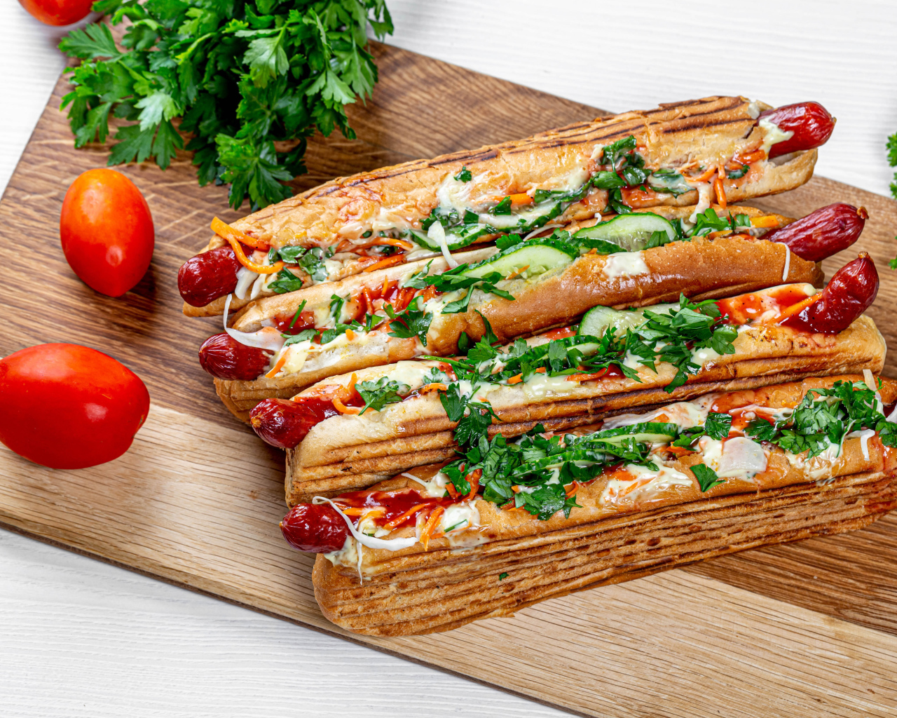 Hot dogs on a board with parsley and red tomatoes and parsley