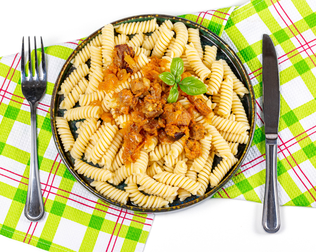 Большая тарелка макарон с мясом на столе со столовыми приборами