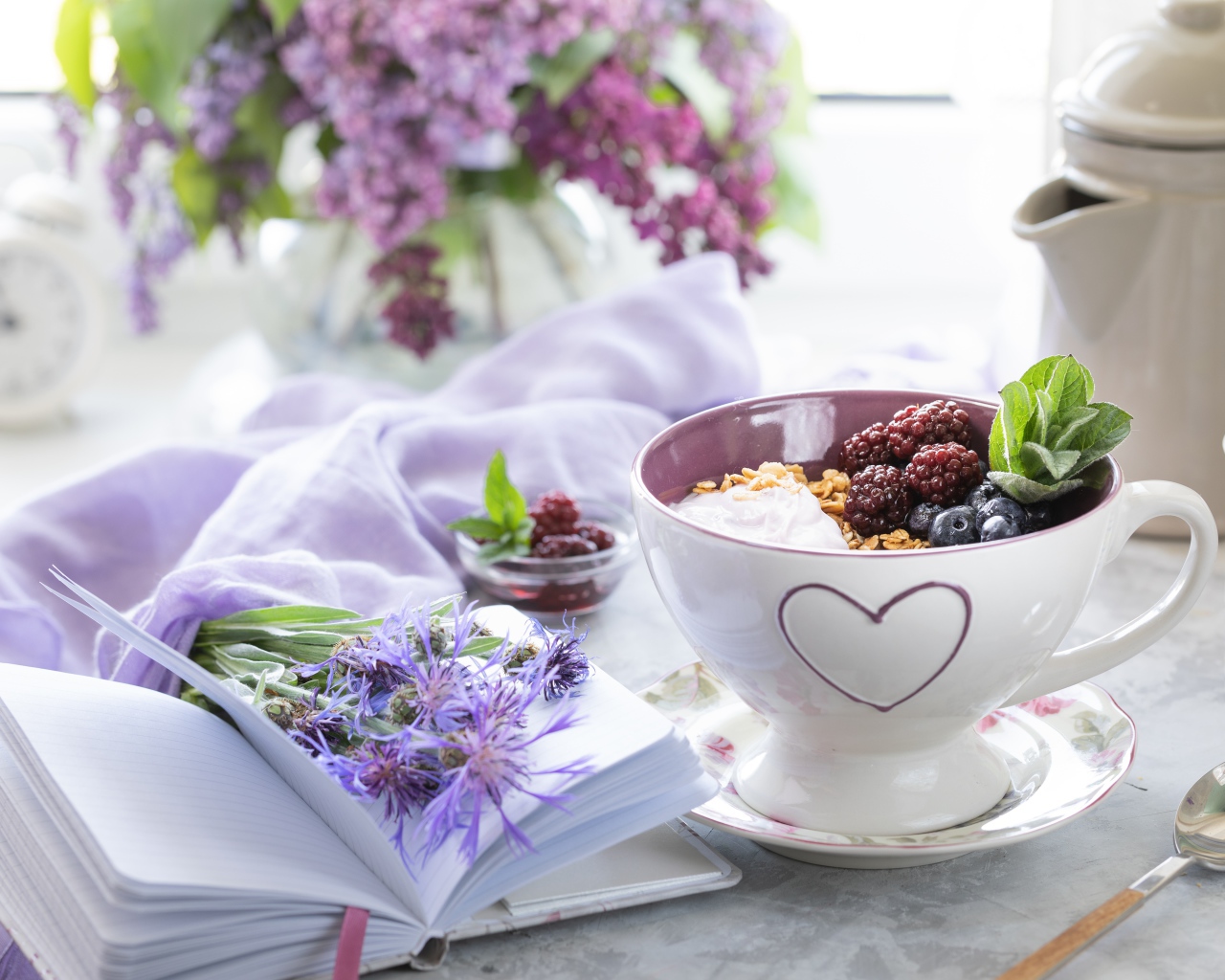 Мюсли с ягодами в чашке на столе с блокнотом и букетом сирени 